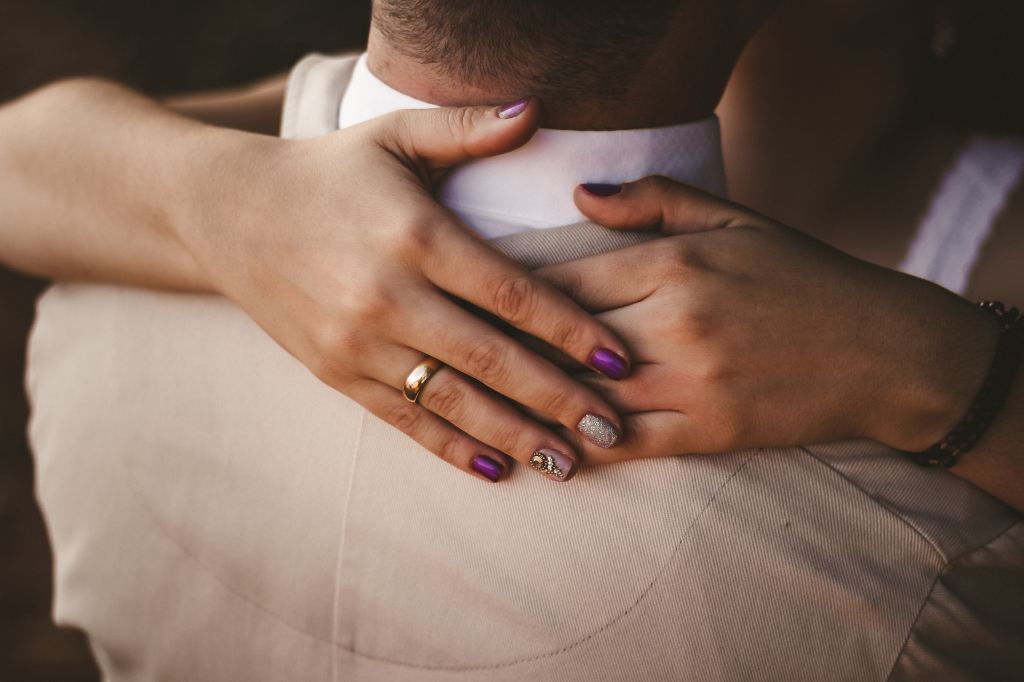 A brides arms wrapped around her groom, showing off her wedding ring
