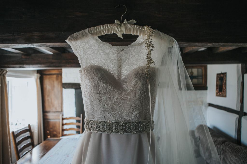 A white lace wedding dress hanging from the beams of an old english-style home.