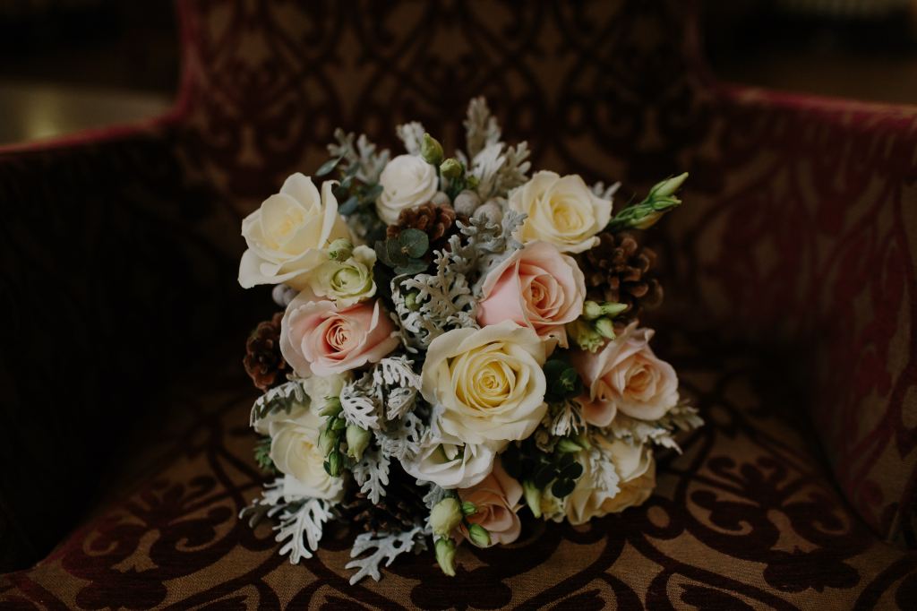 A bouquet consisting of pink and yellow, frosted oak leaves, and pine-cones.