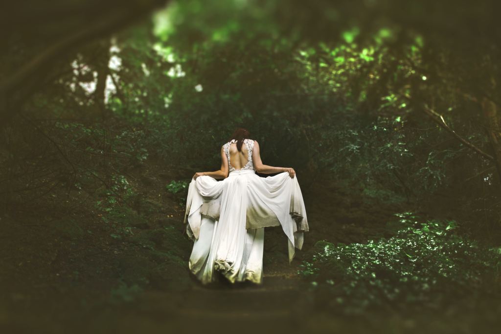 A bride ascending stairs in a forest.