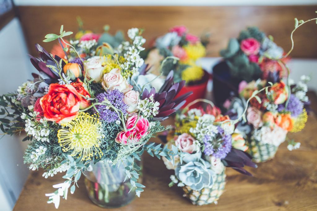 A bright series of bouquets consisting of wildflowers, roses, and succulents, some with bases of pineapples.