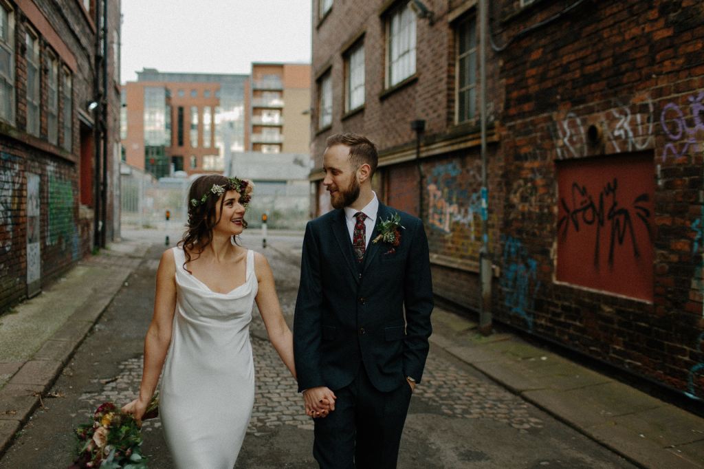 A bride and groom happily walking through an urban brick alley with graffiti on the walls.
