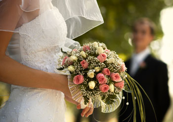 A bride wearing a white dress with her veil down holding a bouquet of pink and yellow roses.